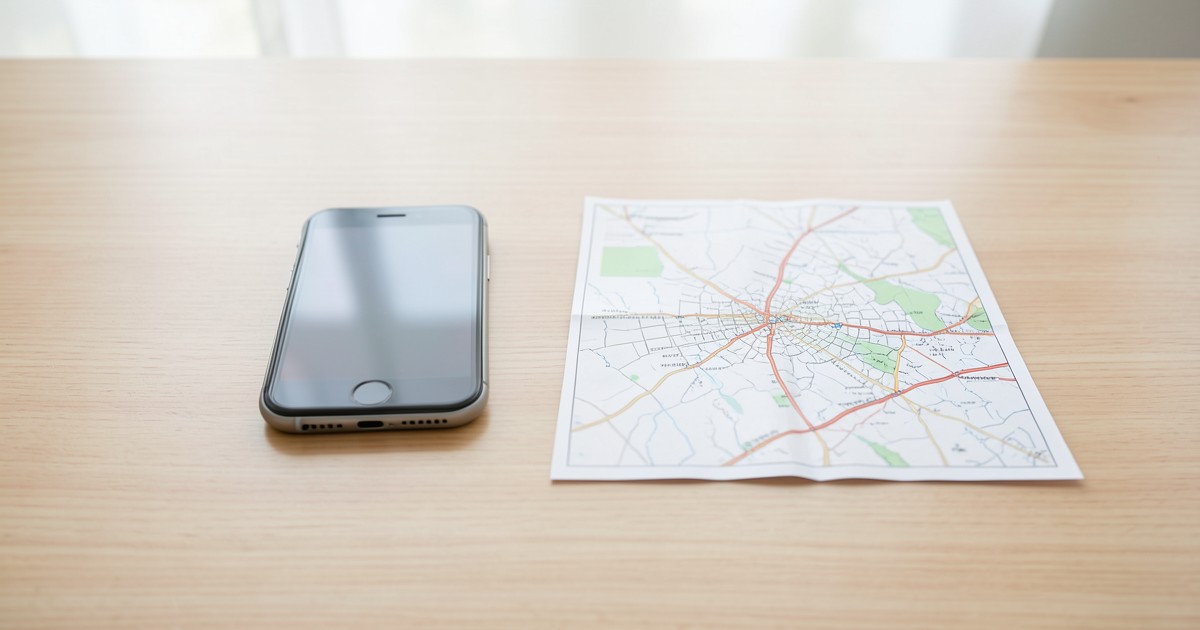 机の上に置かれたスマートフォンと地図の画像。情報の収集とコミュニティの計画を象徴しています。